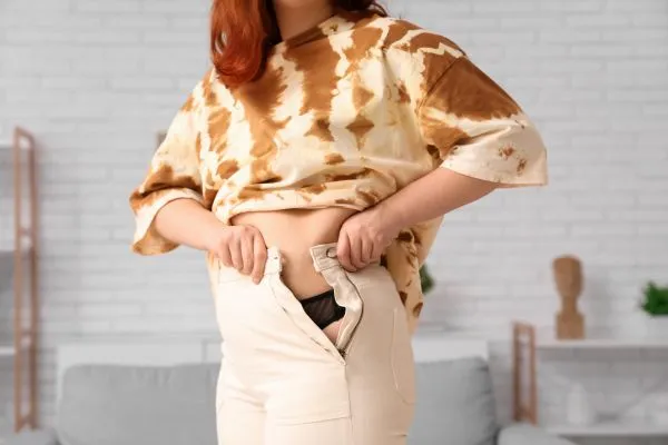 Image of woman trying to do her trousers up after pregnancy weight gain Lancaster
